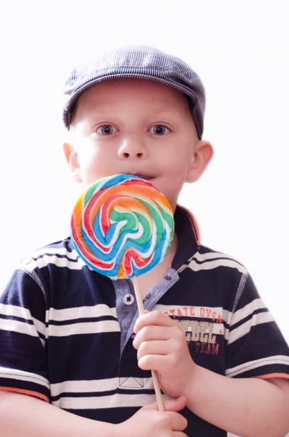 Un petit garçon avec un béret mange une sucette multicolore. 